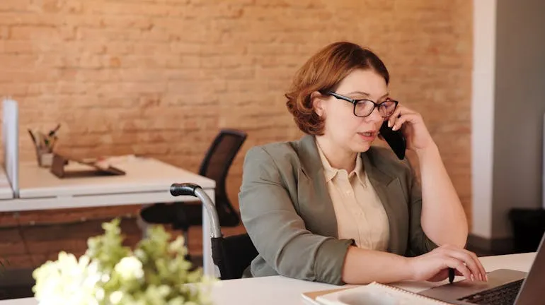 Woman Talking Through Smartphone While Using Laptop