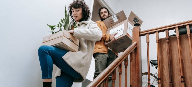 Couple Going Down The Stairs With Box Of Books And Plants