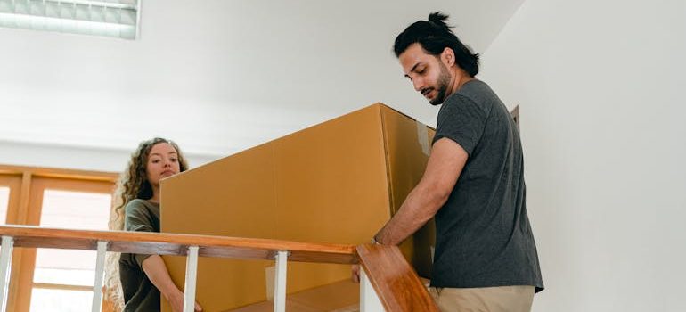 Couple carrying big carton box in direction of stairs
