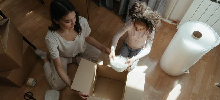 Woman in Gray Shirt Sitting on Floor Beside Girl in White Shirt
